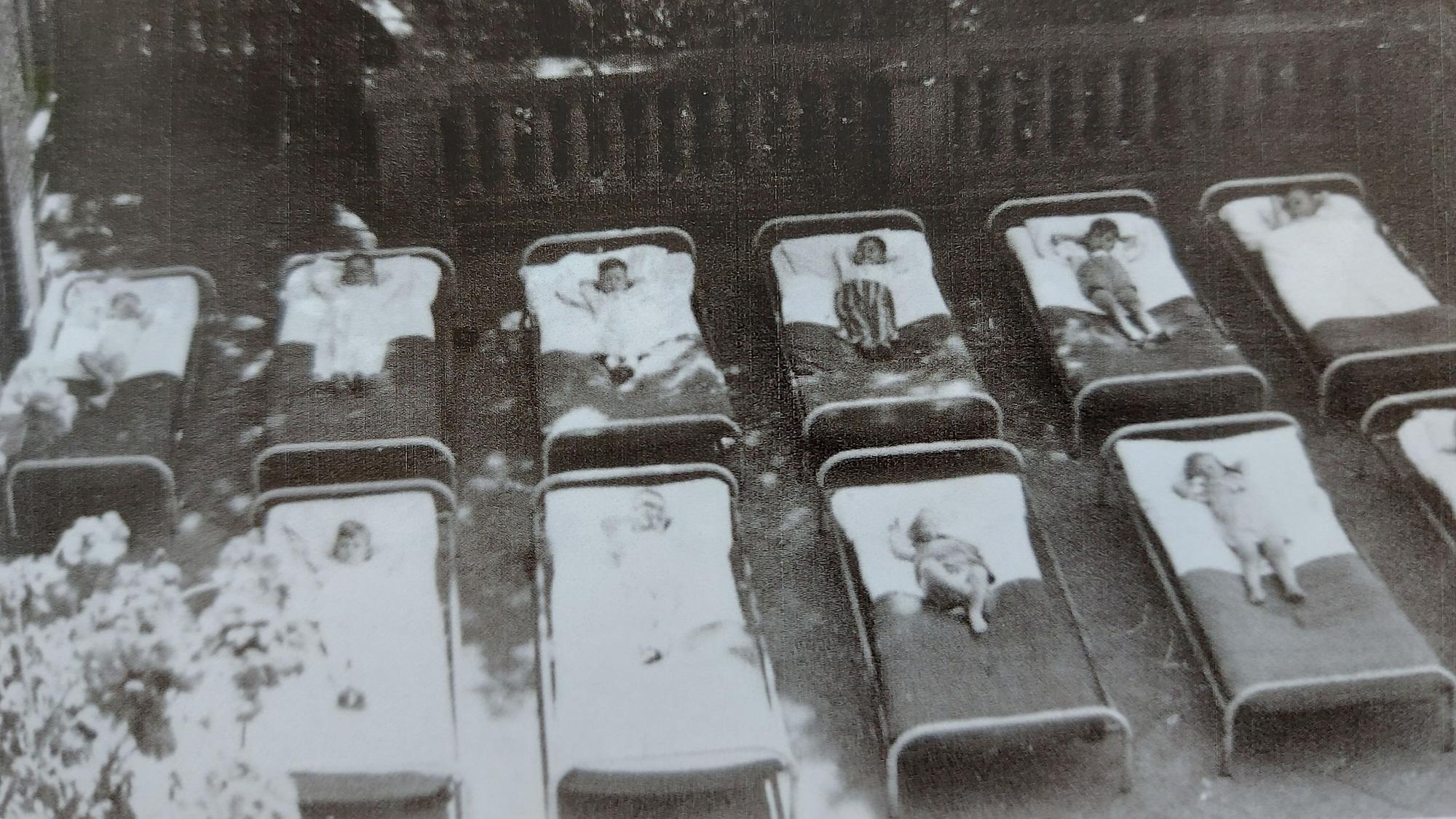 10 Kinder liegen in sorgsam aufgereihten Krankenbetten auf einer Terrasse.