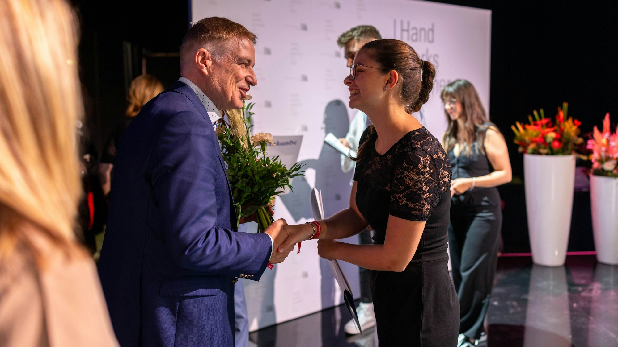 Theresa Spies erhält die Ehrenurkunde der Handwerkskammer zu Köln, ein Mann gratuliert ihr.