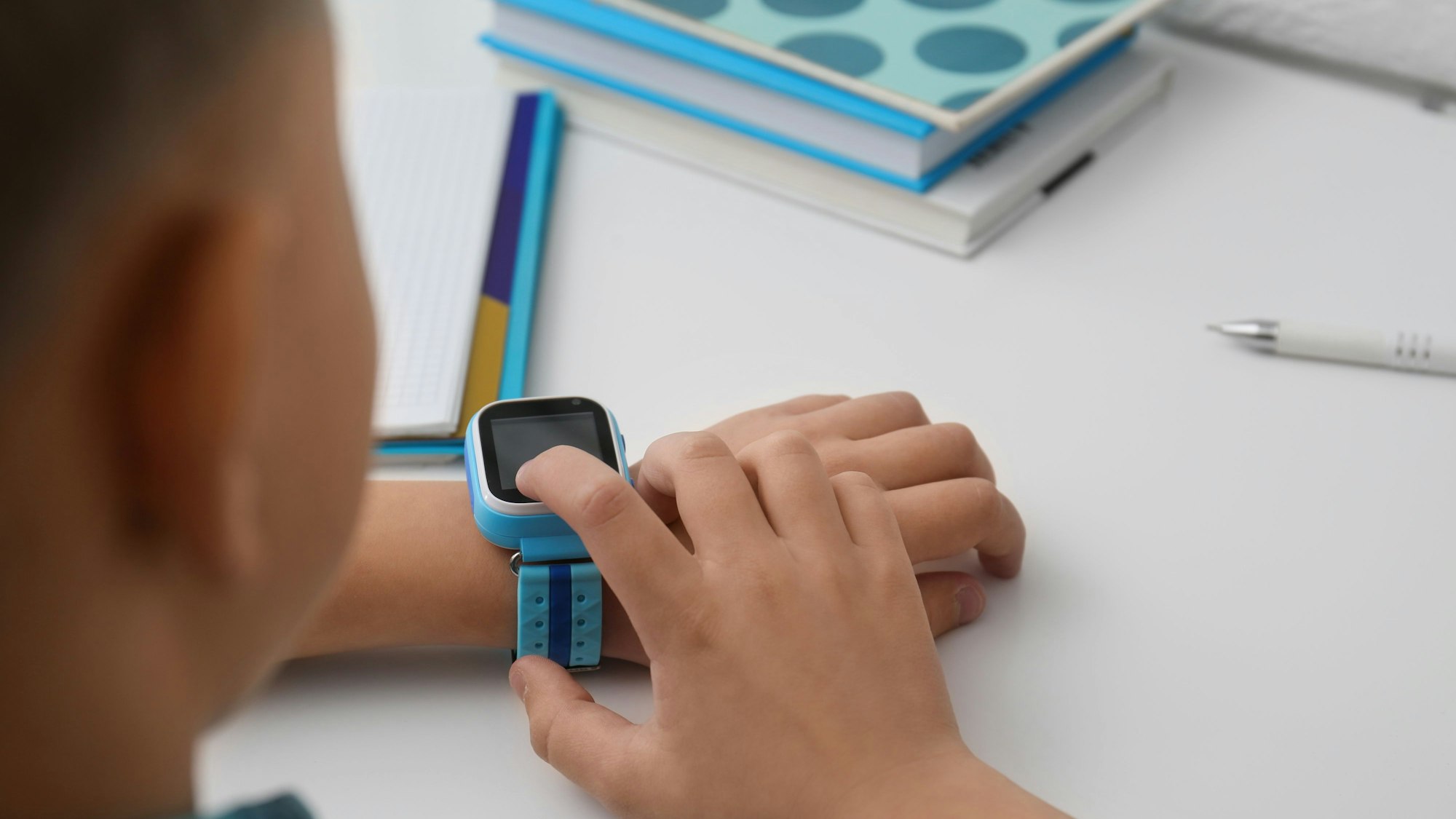 Boy with stylish smart watch at white table, closeup
