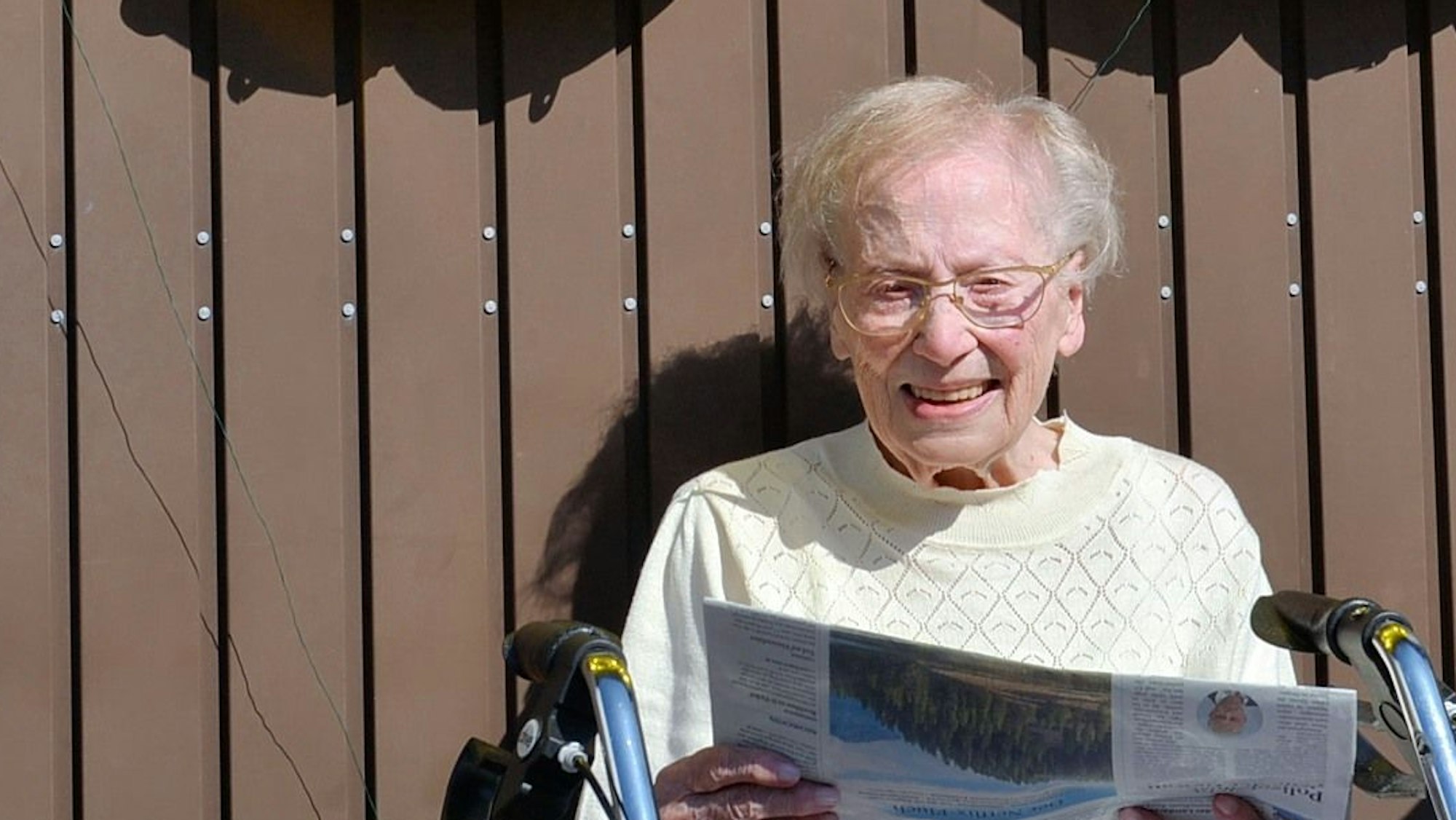 Eine ältere Frau sitzt auf einem Rollator in der Sonne und liest Zeitung