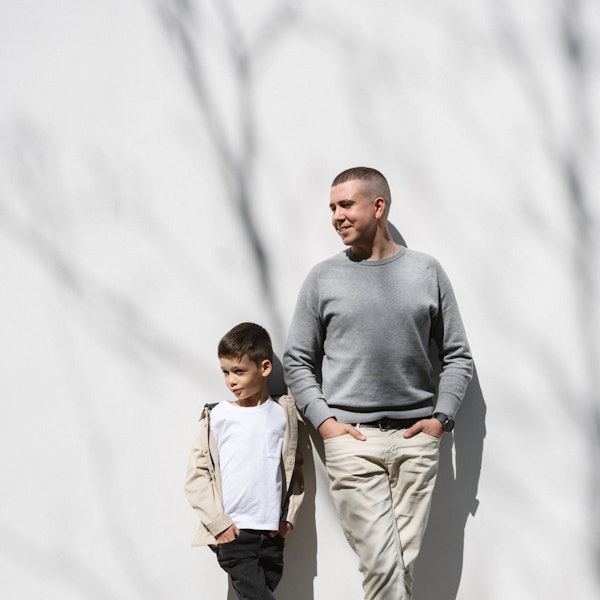 Ein Mann und ein kleiner Junge lehnen sich gemeinsam an eine weiße Wand an.