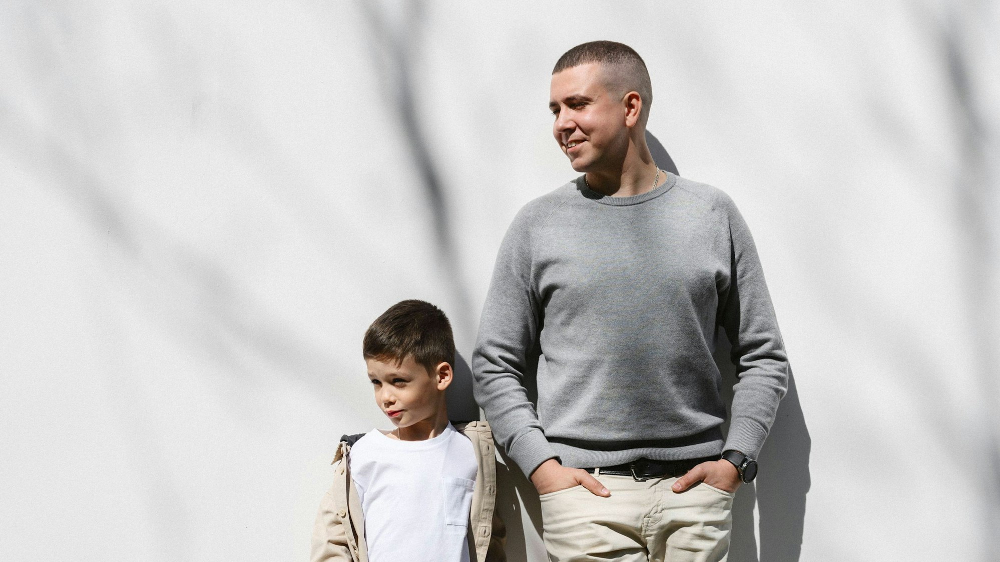 Ein Mann und ein kleiner Junge lehnen sich gemeinsam an eine weiße Wand an.