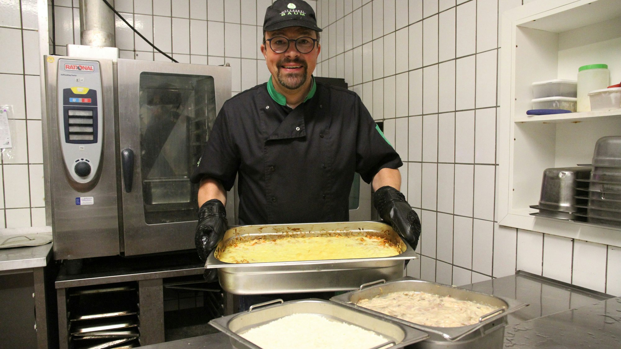 Ein Mann hält in einer Profiküche eine Auflaufform in den Händen.