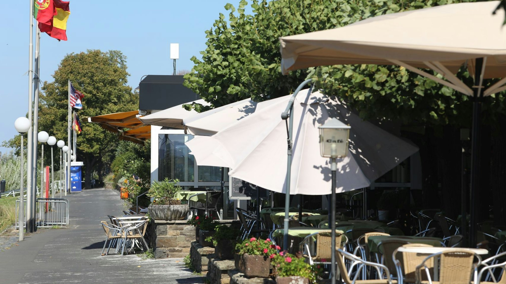 Tische und Stühle sowie Sonnenschirme einer Außengastronomie an der Rheinpromenade.