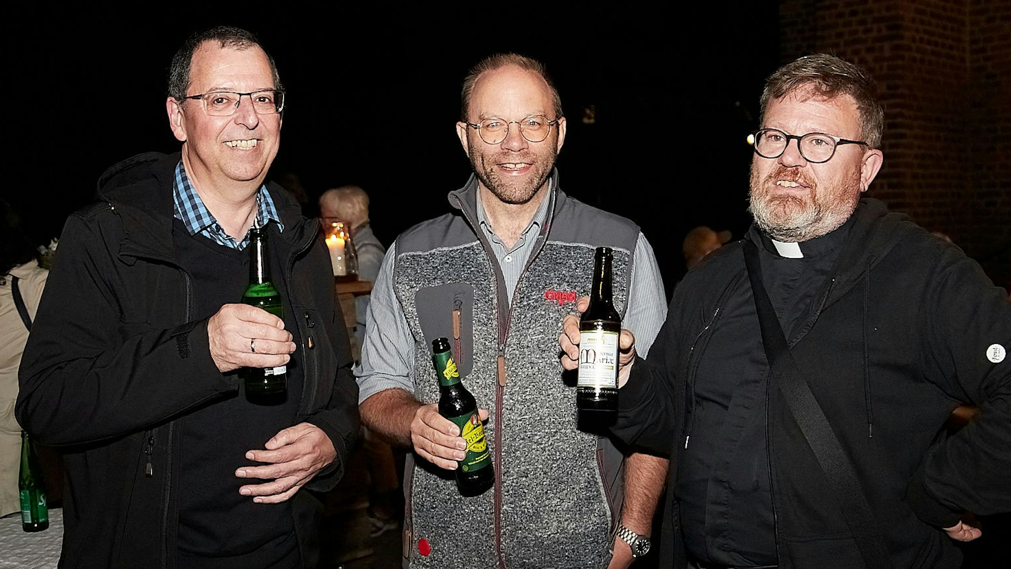 Andreas Warler, Jörg Lenzen und Michael Krosch stehen beieinander und stoßen mit Bierflaschen an.