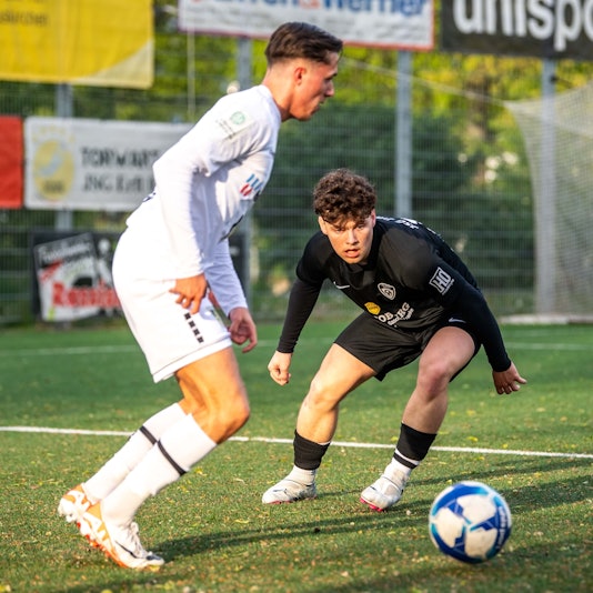Ein Fußballspieler schaut gebannt auf einen Ball, der von einem Gegenspieler geführt wird.
