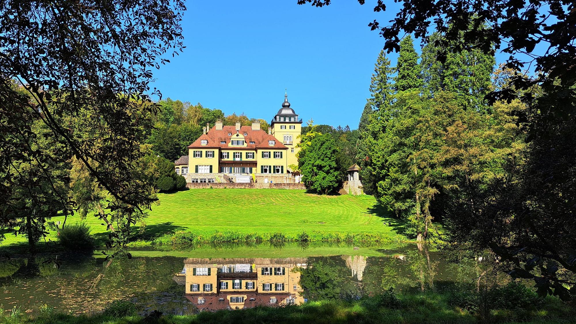 Schlosshotel Lerbach ist hinter dem Schlossteich zwischen Bäumen zu sehen.