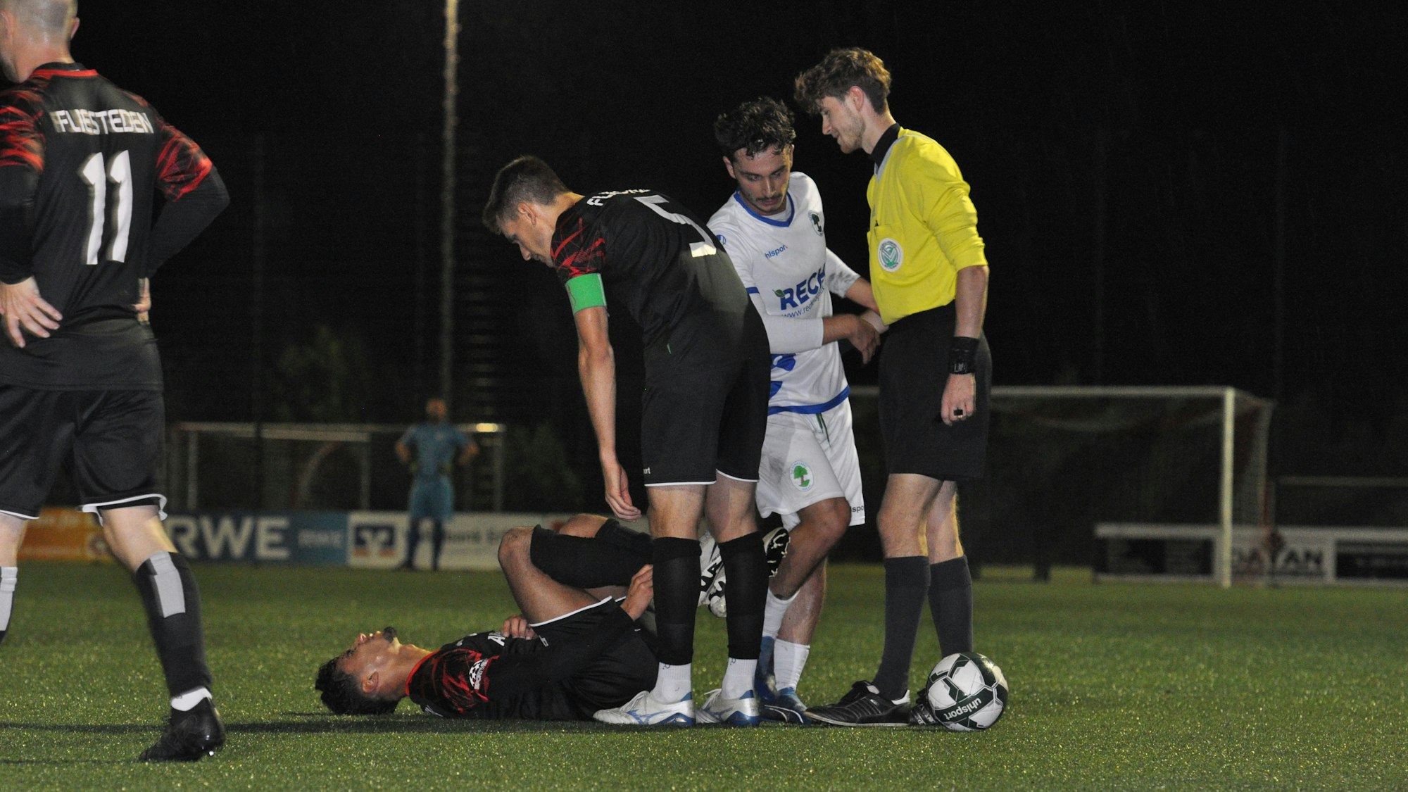 Ein Fußballspieler liegt am Boden, andere Spieler stehen daneben.
