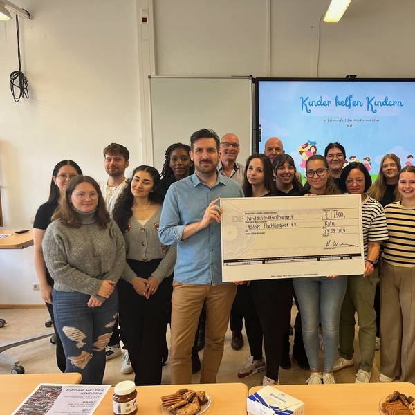 Schülerinnen und Schüler des Joseph-DuMont-Berufskollegs übergeben Jashar Erfanian vom Kölner Flüchtlingsrat einen symbolischen Scheck in Höhe von 2500 Euro.