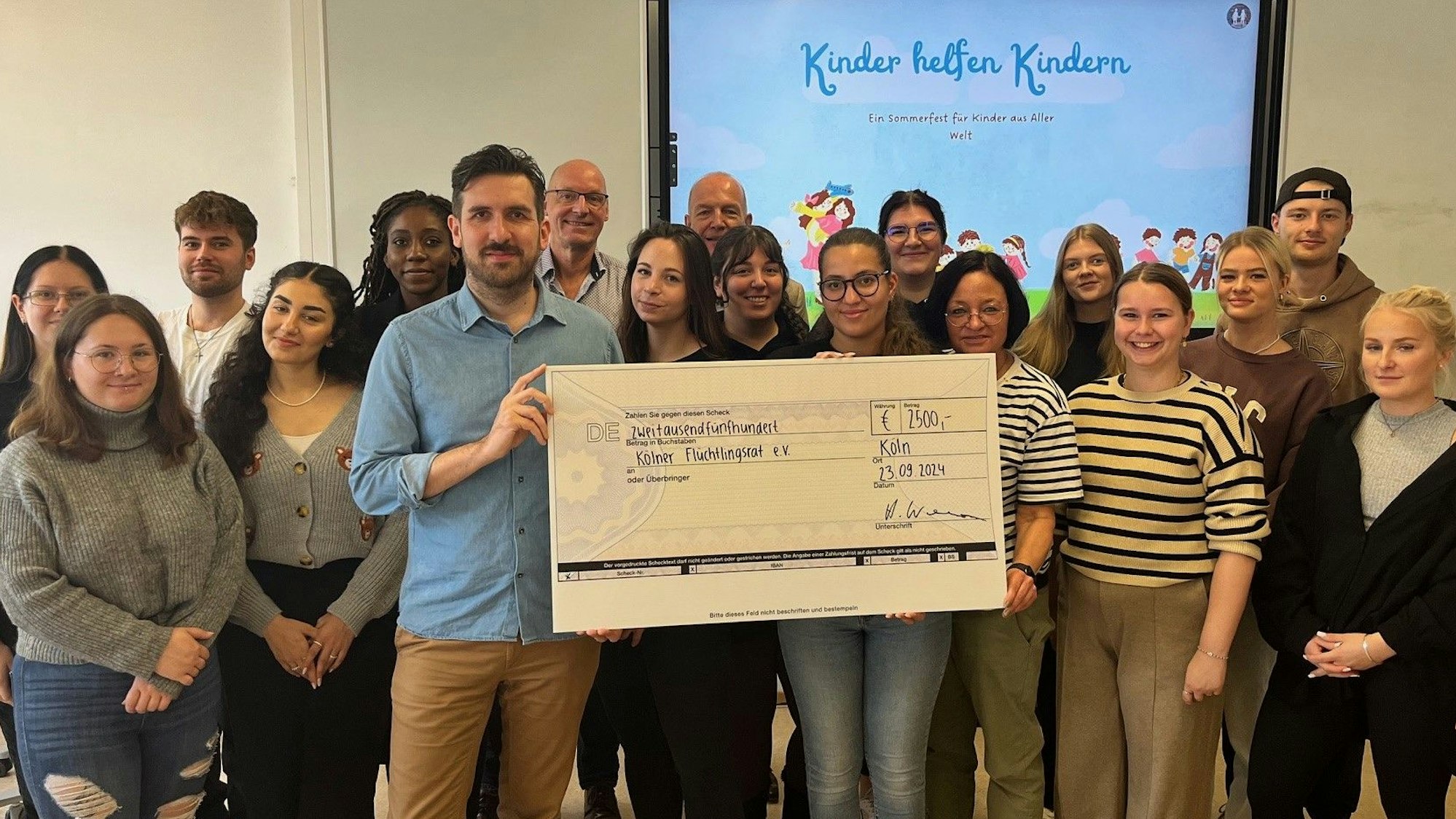 Schülerinnen und Schüler des Joseph-DuMont-Berufskollegs übergeben Jashar Erfanian vom Kölner Flüchtlingsrat einen symbolischen Scheck in Höhe von 2500 Euro.