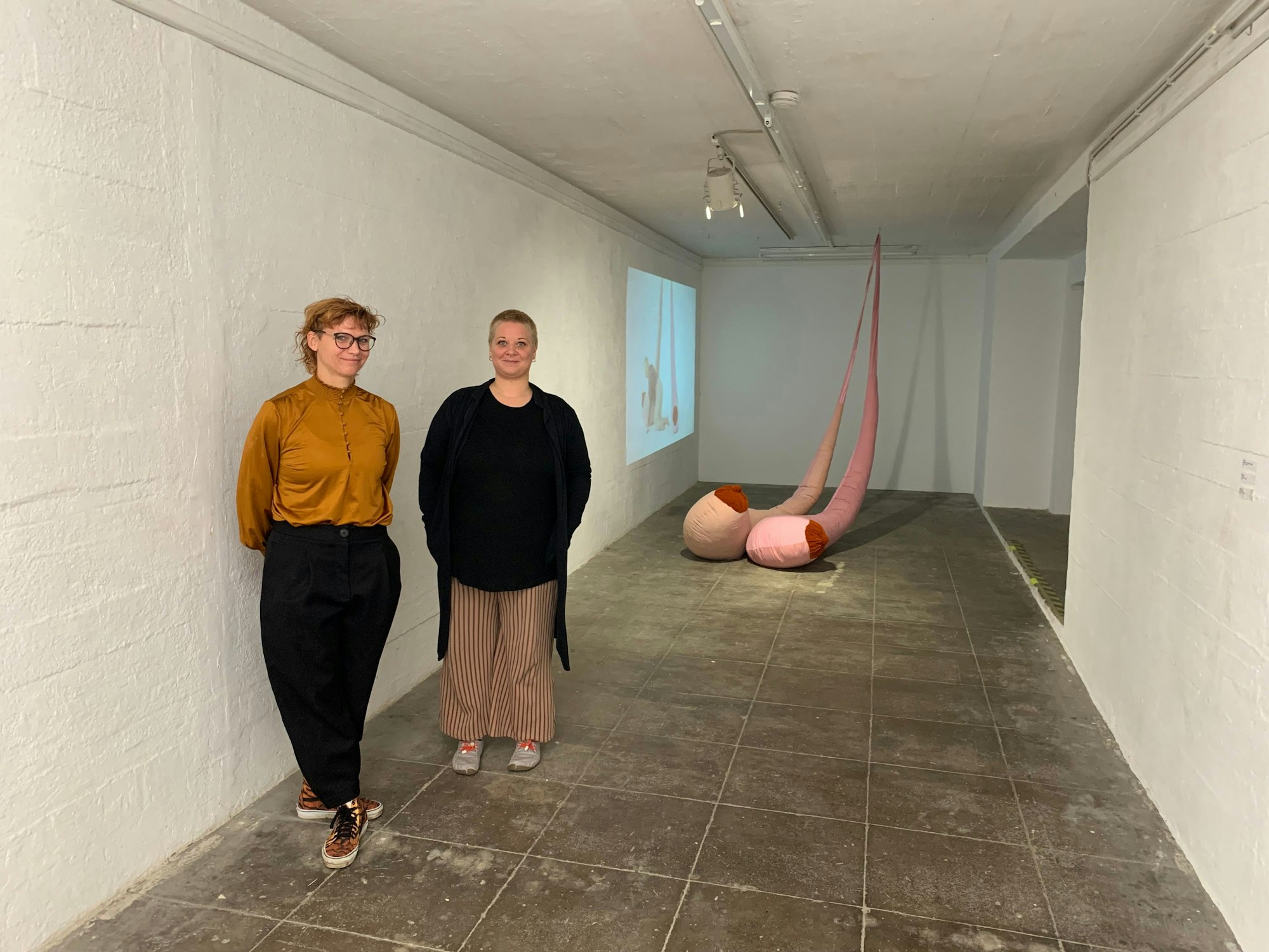 Zwei Frauen stehen in einem Raum mit einem Kunstwerk.