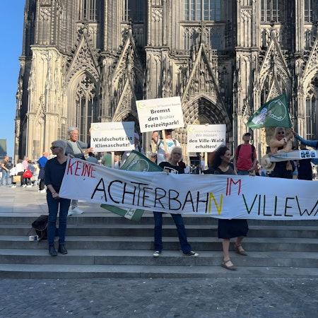 Zu sehen sind die Aktiven des Klimabündnisses, die ein großes Transparent mit der Aufschrift „Keine Achterbahn im Villewald“ halten.