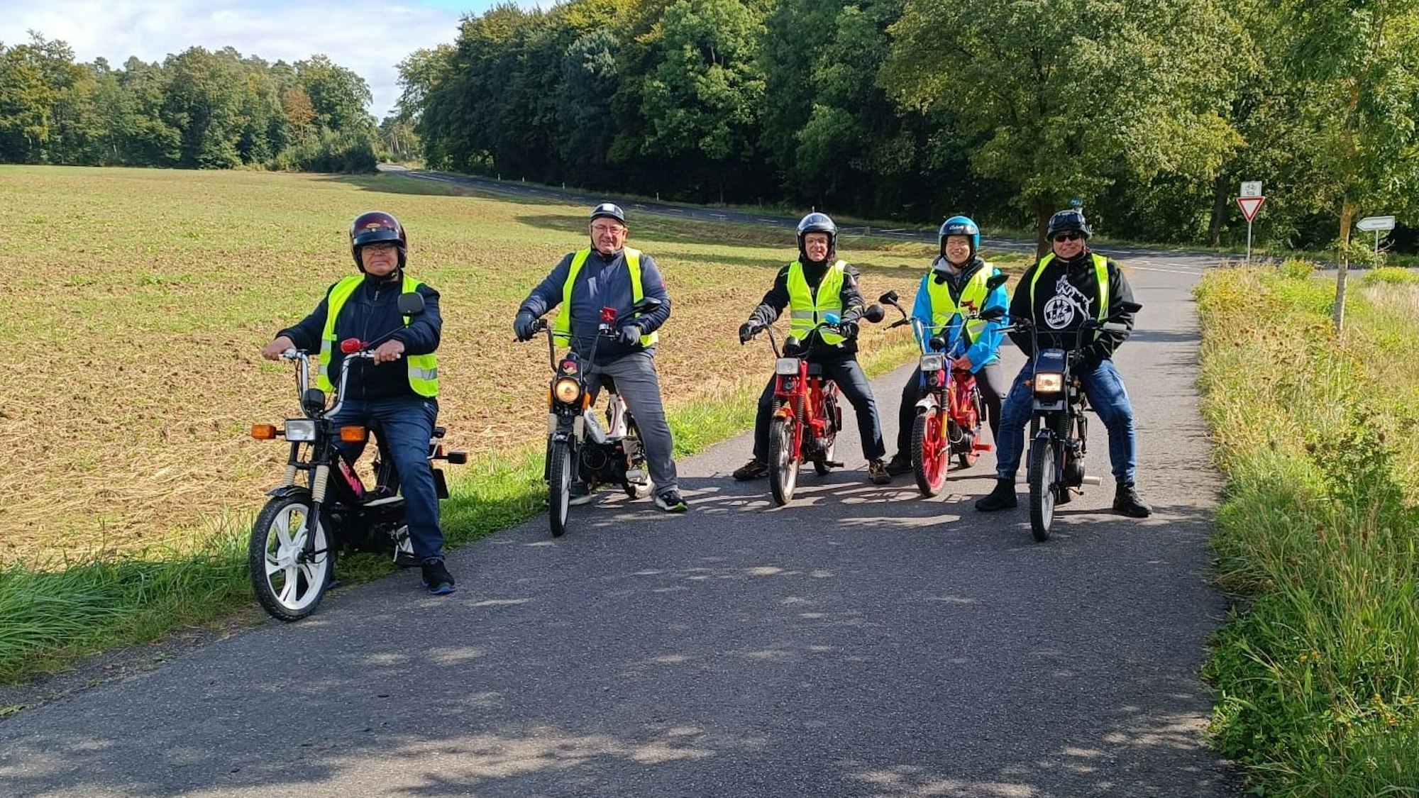 Fünf Männer mit Helm und Warnweste sitzen auf historischen Mopeds