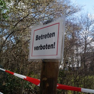 Ein „Betreten verboten!“-Schild hängt an einem Pfahl, dahinter ist rotweißes Flatterband zu sehen.