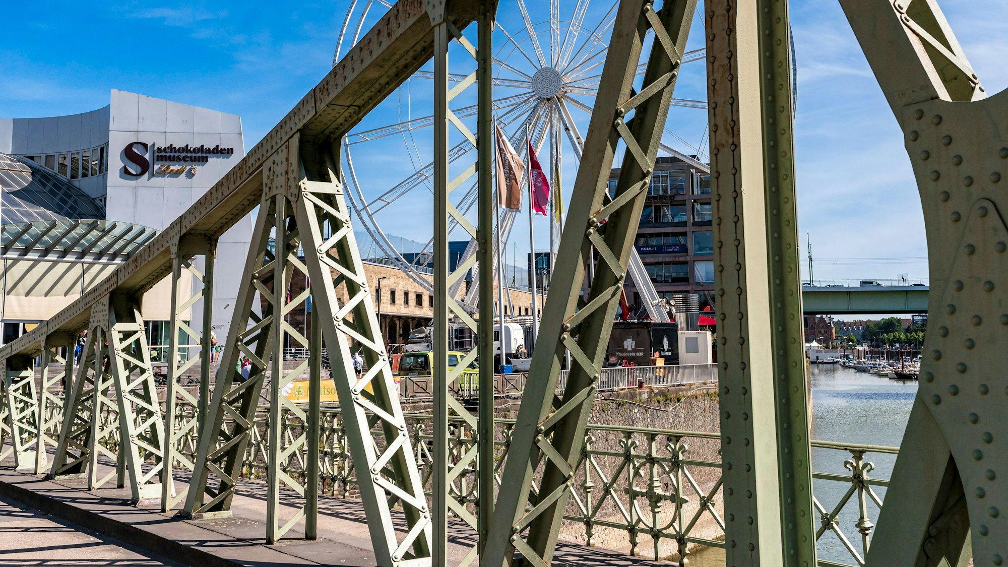 Zu sehen ist die Drehbrücke, die zum Kölner Schokoladenmuseum führt. Im Hintergrund sind das Museum, ein Riesenrad und ein Teil der Severinsbrücke zu sehen.