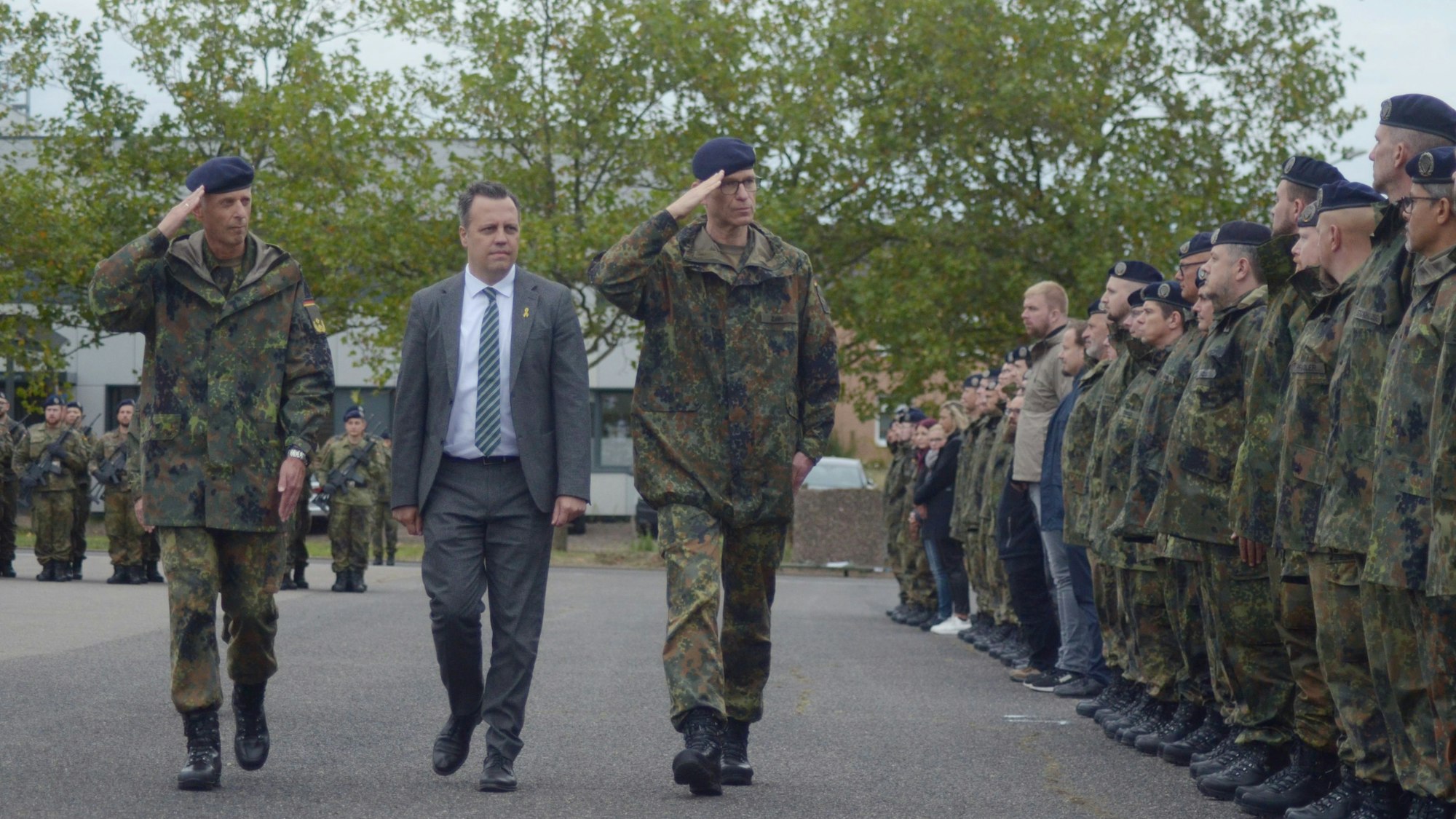 Drei Männer gehen nebeneinander an den Frauen und Männern entlang, die in einer langen Reihe Aufstellung genommen haben.