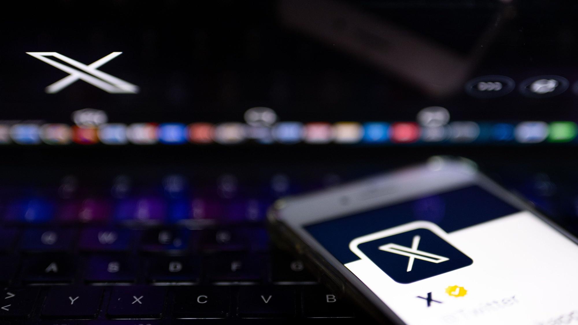 Auf dem offiziellen Profil der Plattform X auf dem Bildschirm eines Smartphones und auf dem Display eines Laptops ist der weiße Buchstabe X auf schwarzem Hintergrund zu sehen.