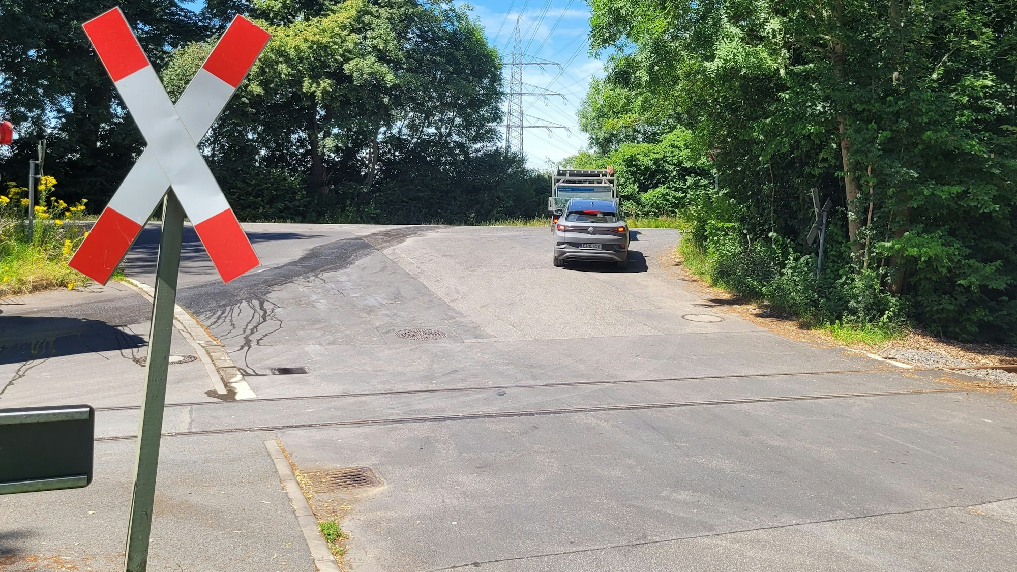 Bahngleise, links ein rot-weißes Kreuz, im Hintergrund Autos.
