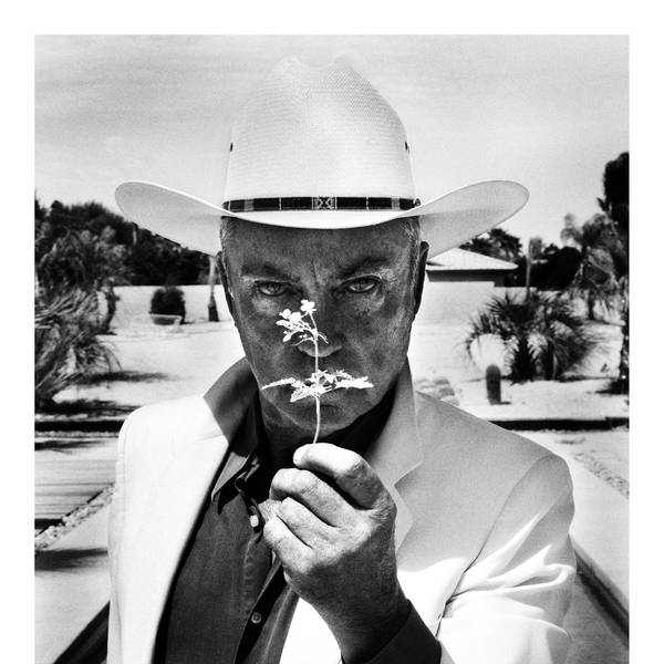 Udo Kier hält eine Blume vor sein Gesicht.