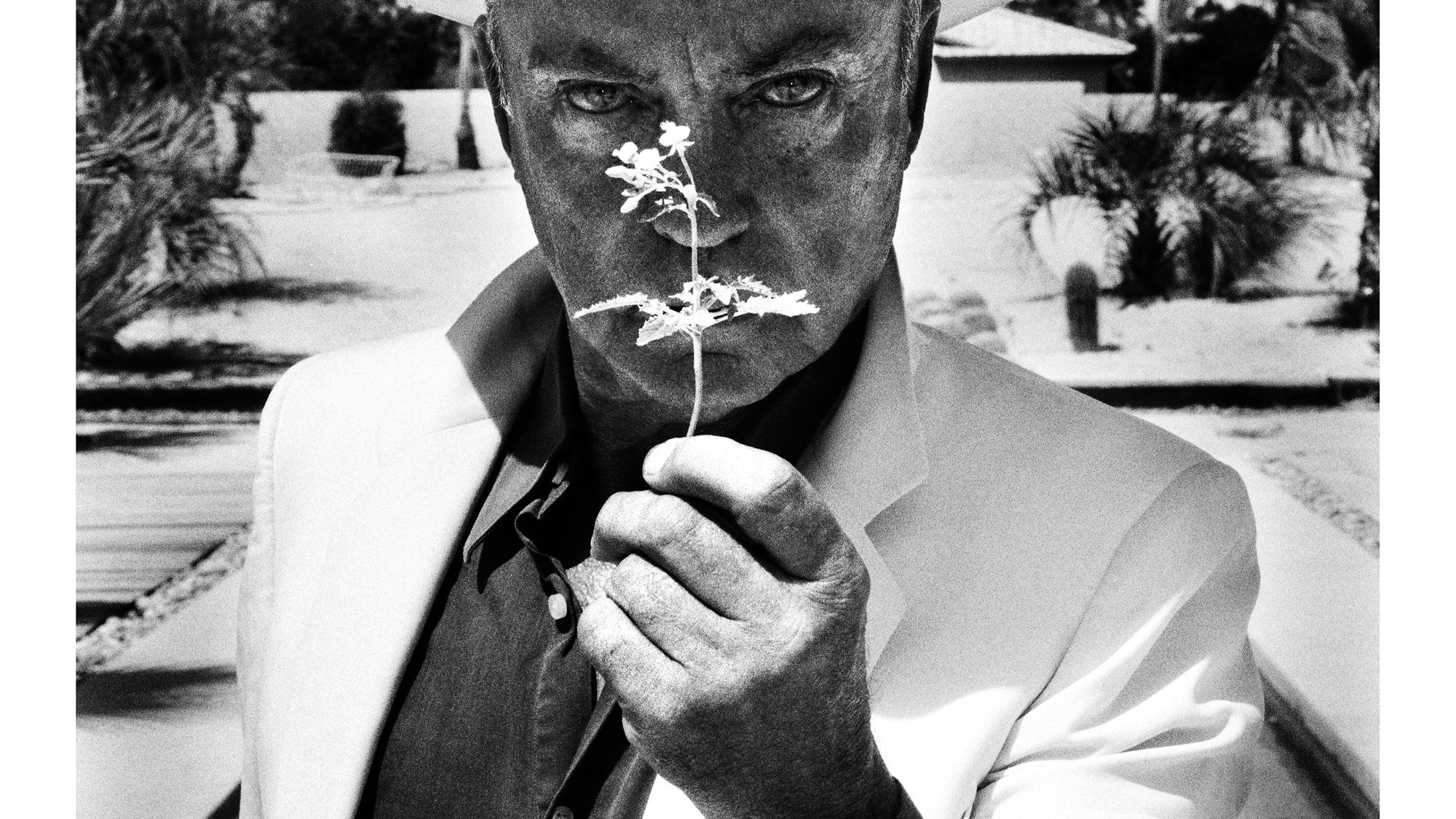 Udo Kier hält eine Blume vor sein Gesicht.