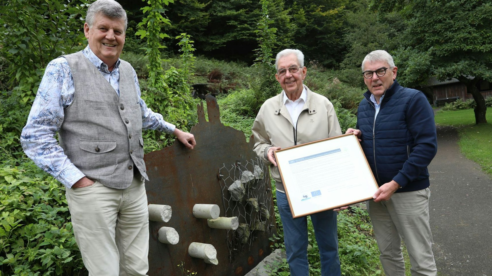 Drei Männer, zwei von ihnen halten einen Bilderrahmen