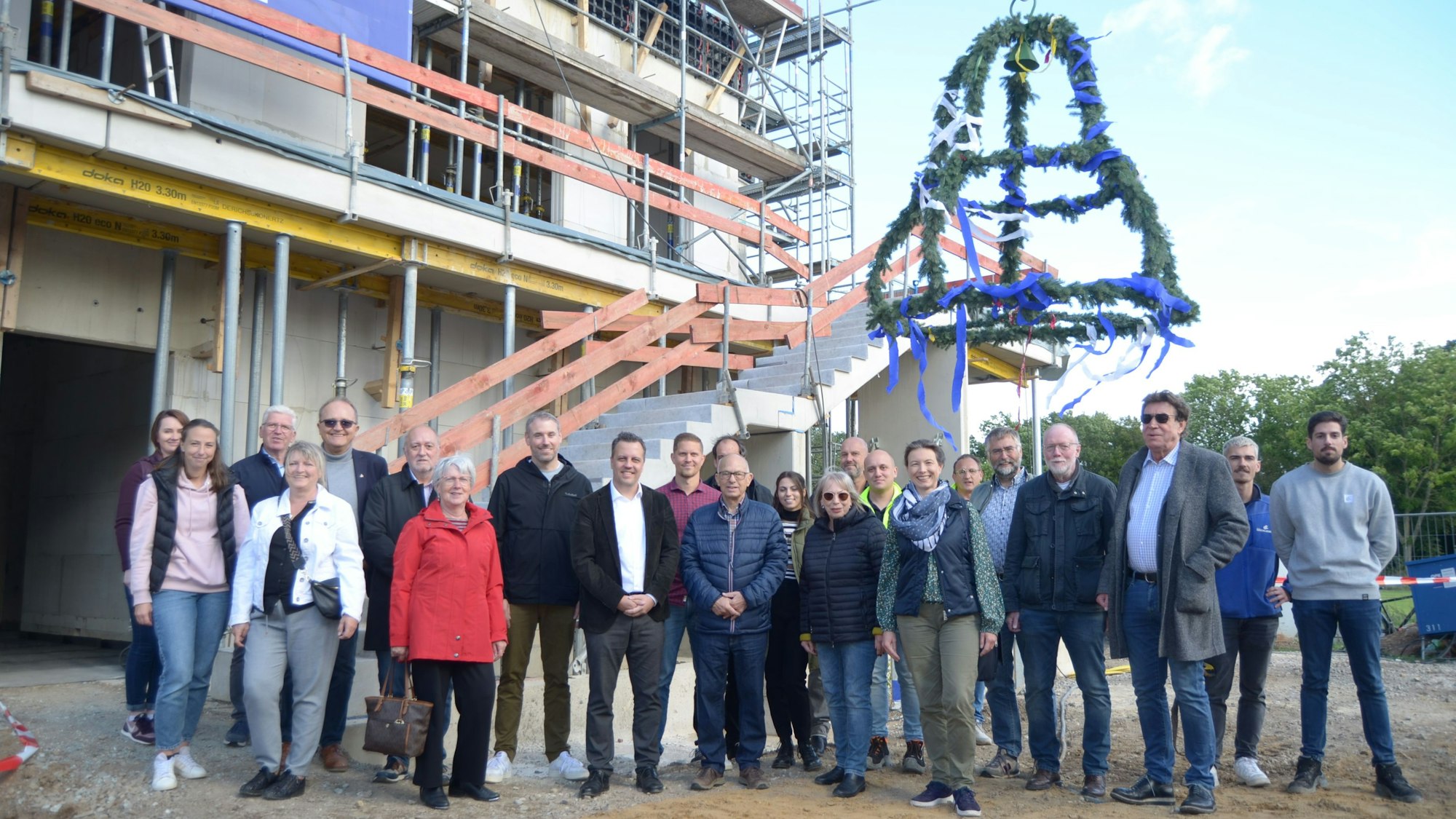 Frauen und Männer stehen vor dem Rohbau, im Hintergrund hängt der Richtkranz.