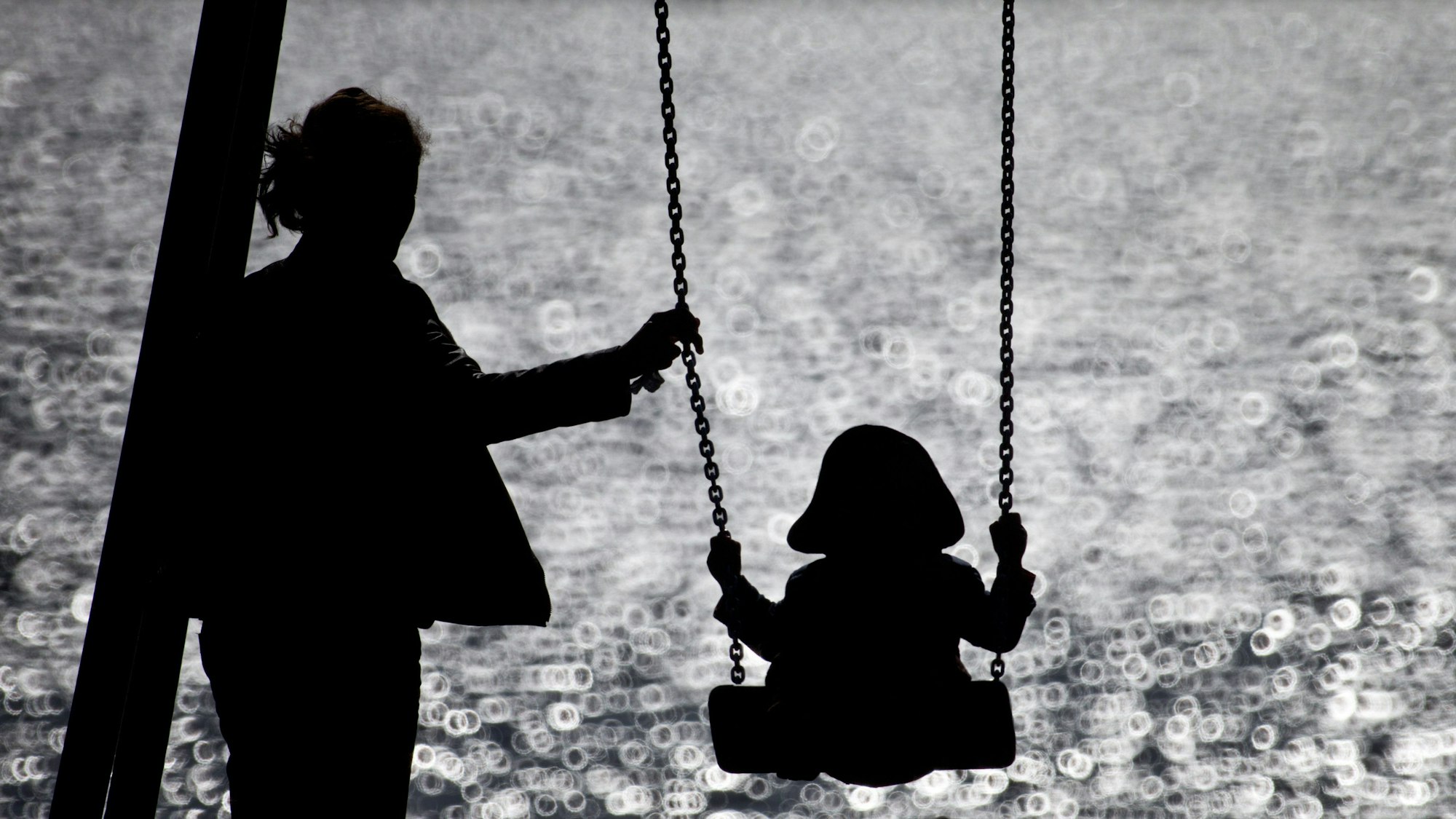 ARCHIV - 16.09.2013, Hamburg: Eine Mutter schaukelt ihr Kind auf einem kleinen Spielplatz am glitzernden Wasser der Alster. (zu dpa: «Anteil Alleinerziehender etwas gesunken - Überwiegend Frauen») Foto: Christian Charisius/dpa +++ dpa-Bildfunk +++