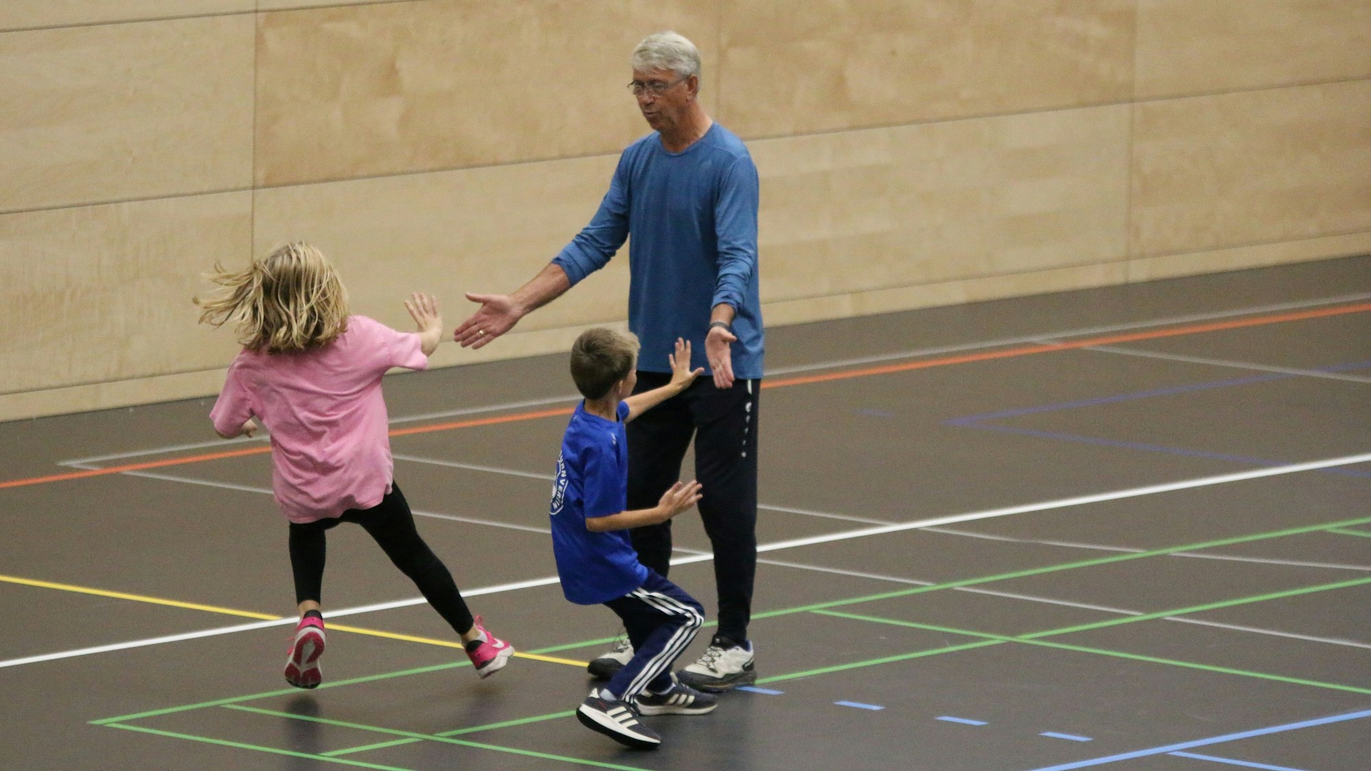 Paul-Heinz Wellmann streckt seine Hände nach außen aus, während zwei Kinder während eines Staffelspiels auf ihn zulaufen, um abzuklatschen.