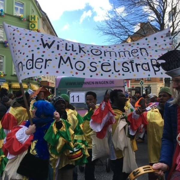 Transparent der Initiative Willkommen in der Moselstraße, im Vordergrund verkleidete Menschen.