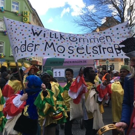 Transparent der Initiative Willkommen in der Moselstraße, im Vordergrund verkleidete Menschen.