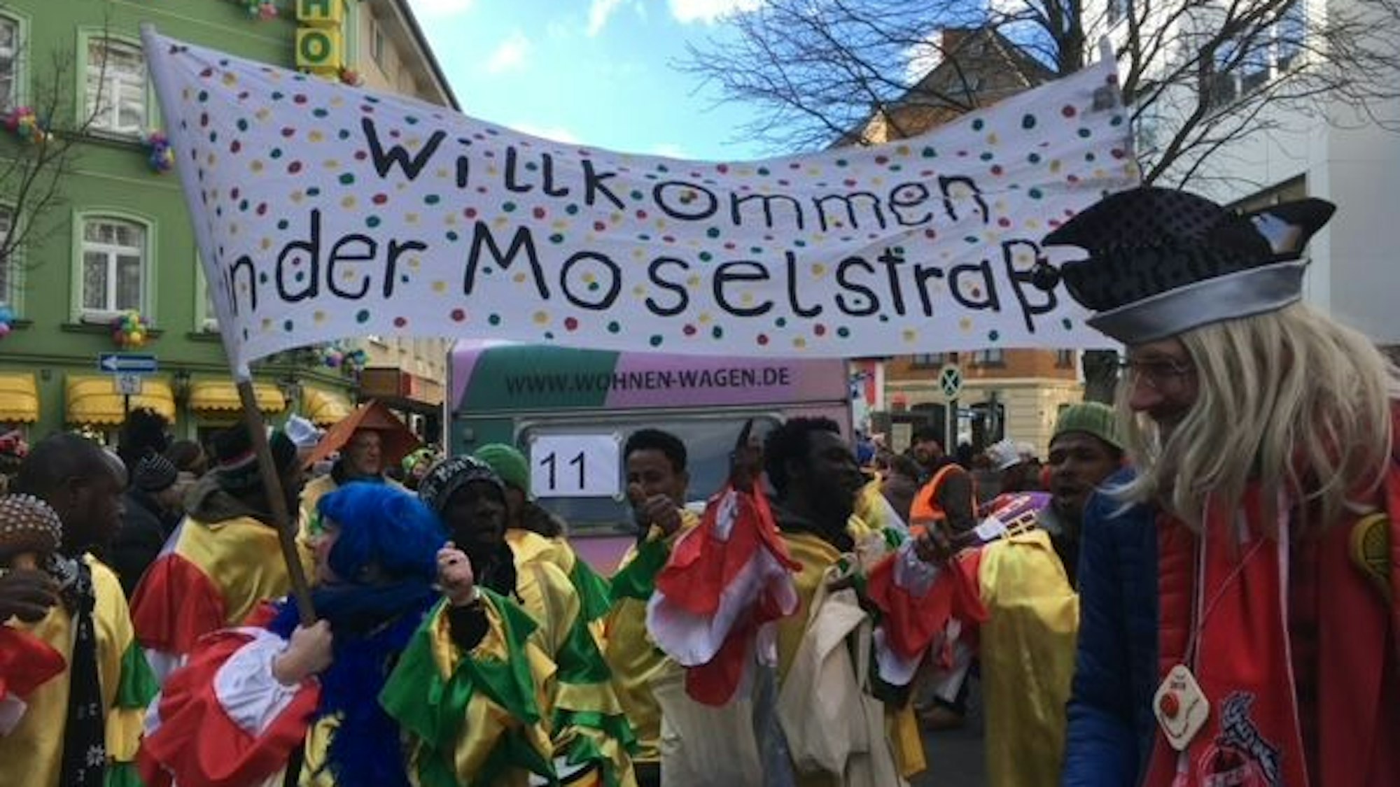 Transparent der Initiative Willkommen in der Moselstraße, im Vordergrund verkleidete Menschen.