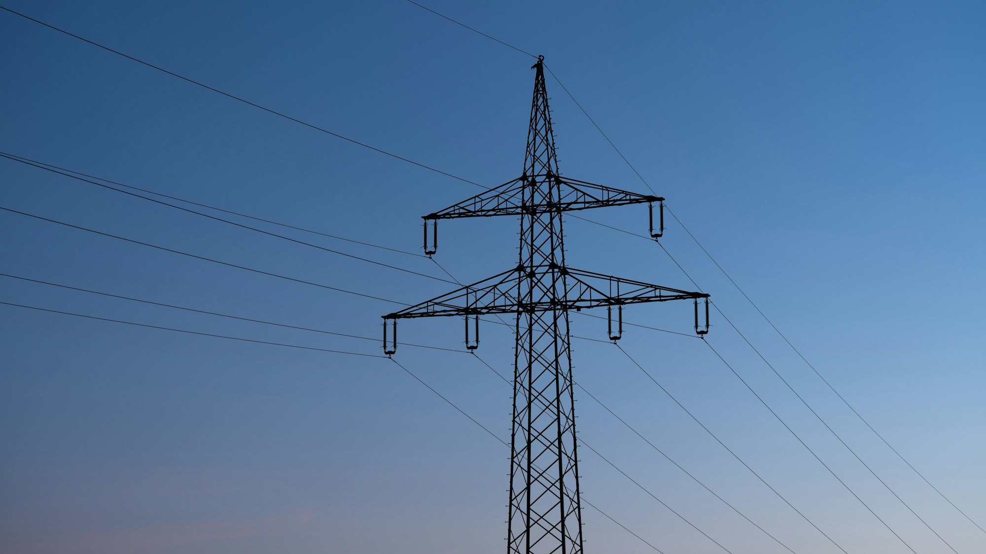 Ein Strommast ist bei Sonnenaufgang als Silhouette zu sehen.