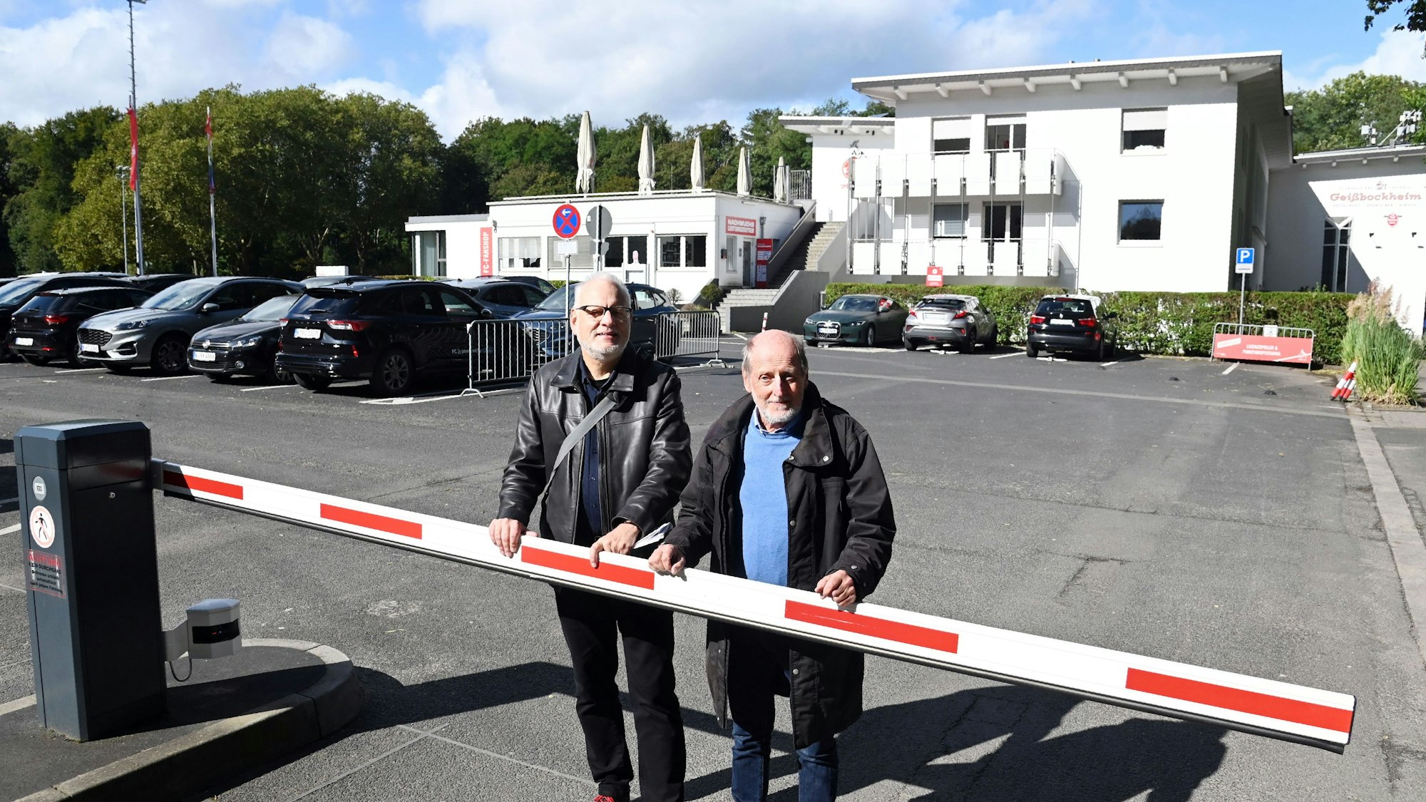 Die beiden Männer stehen auf dem Parkplatz des Geißbockheims.