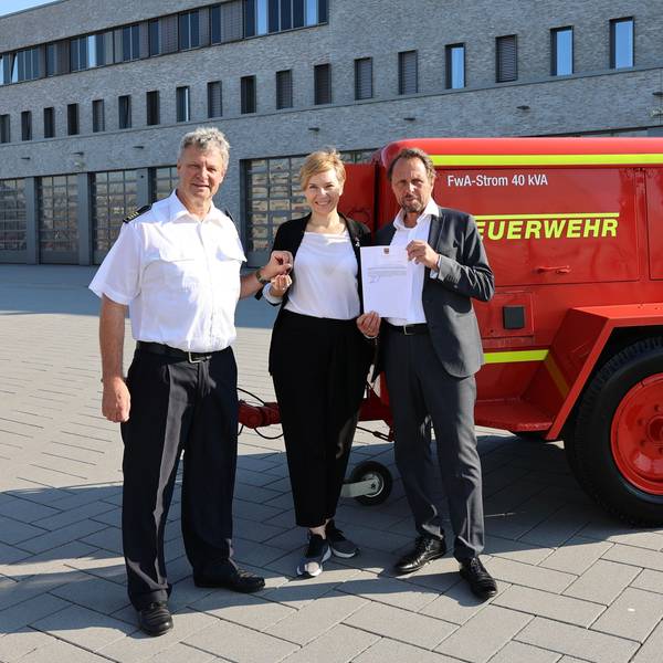 Zwei Männer und eine Frau stehen vor einem Generator.