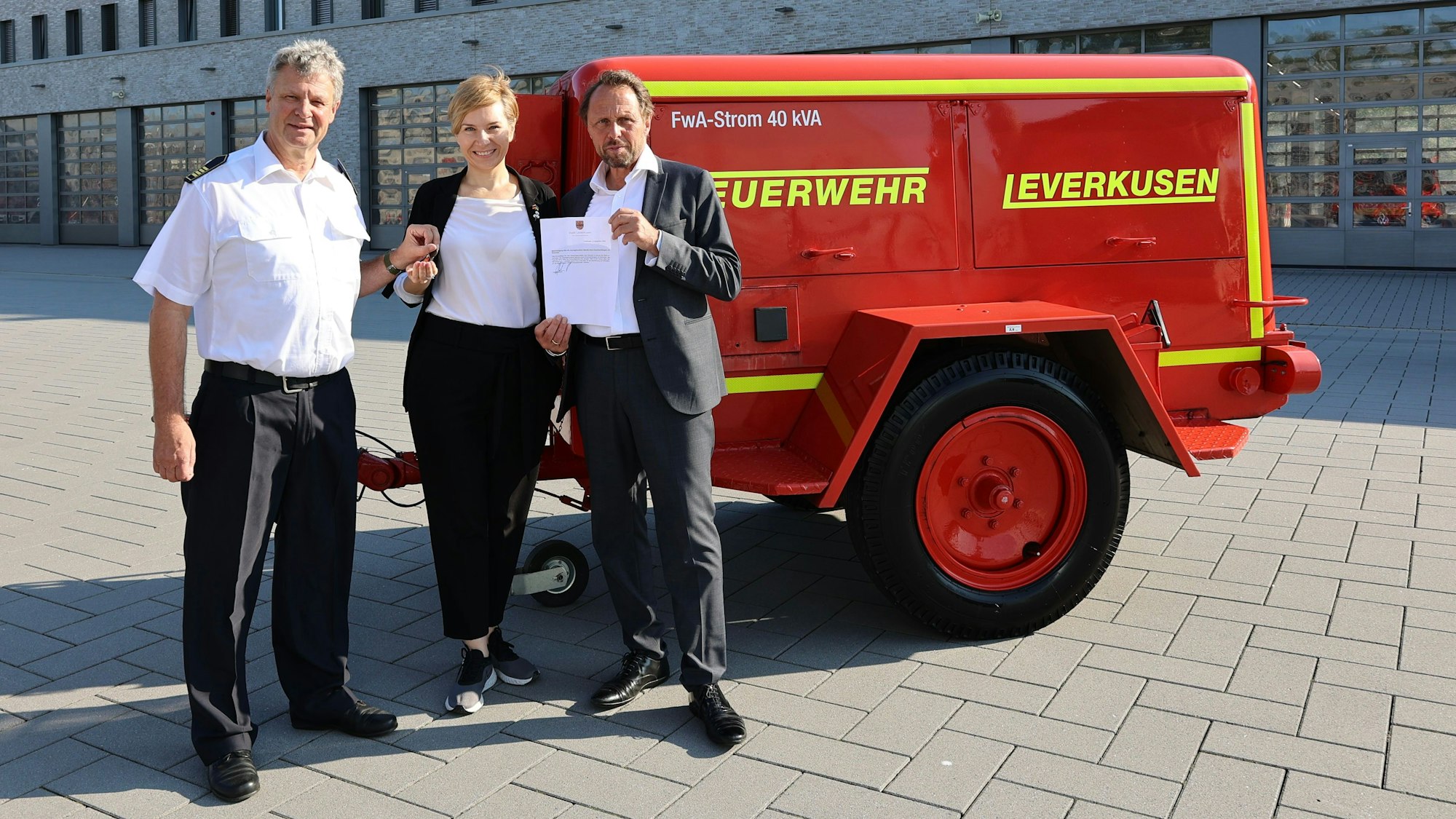 Zwei Männer und eine Frau stehen vor einem Generator.