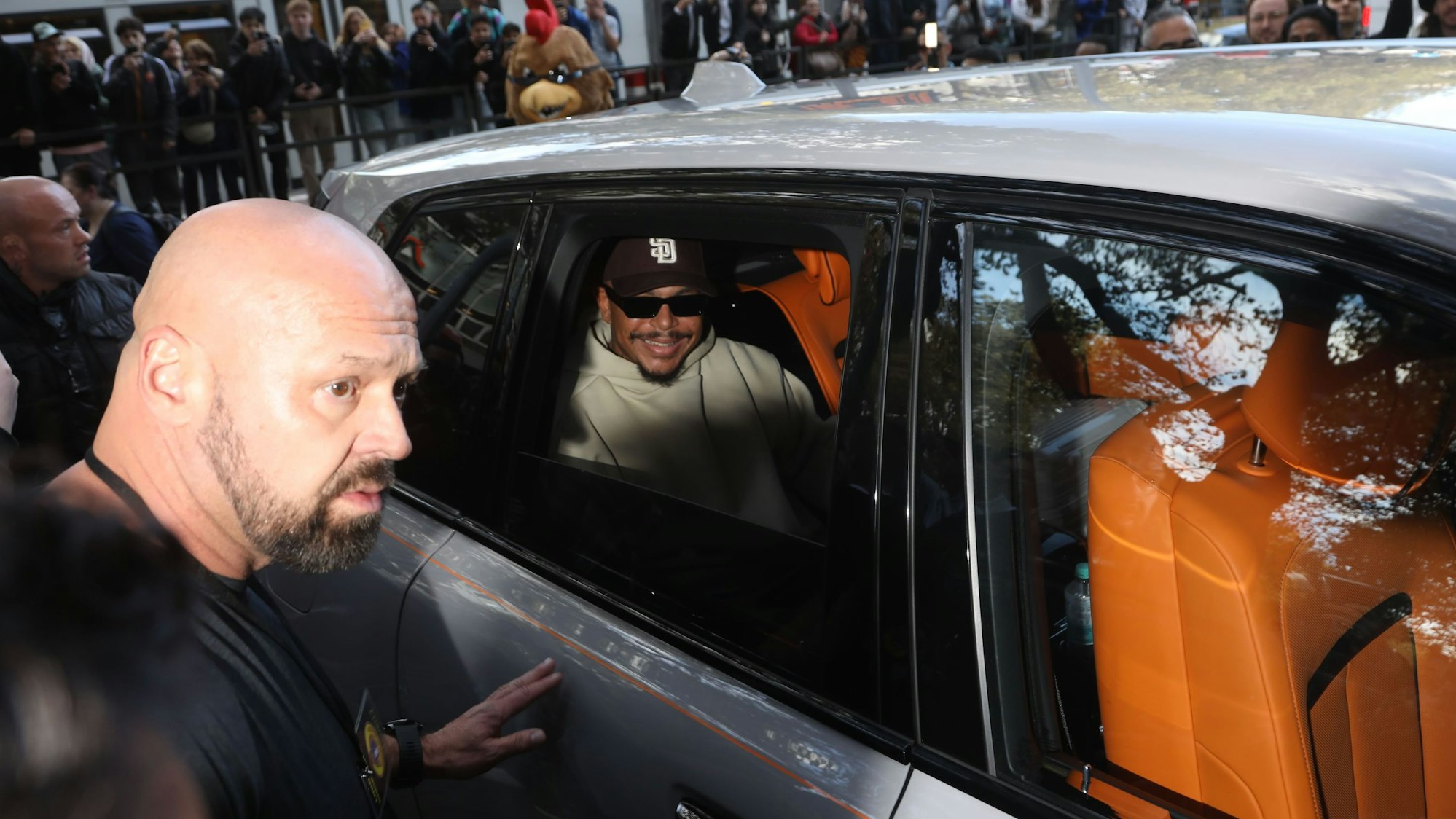 Zu sehen ist der Rapper Luciano auf der Rückbank eines grauen SUVs. Dahinter befindet sich eine große Menschenansammlung.