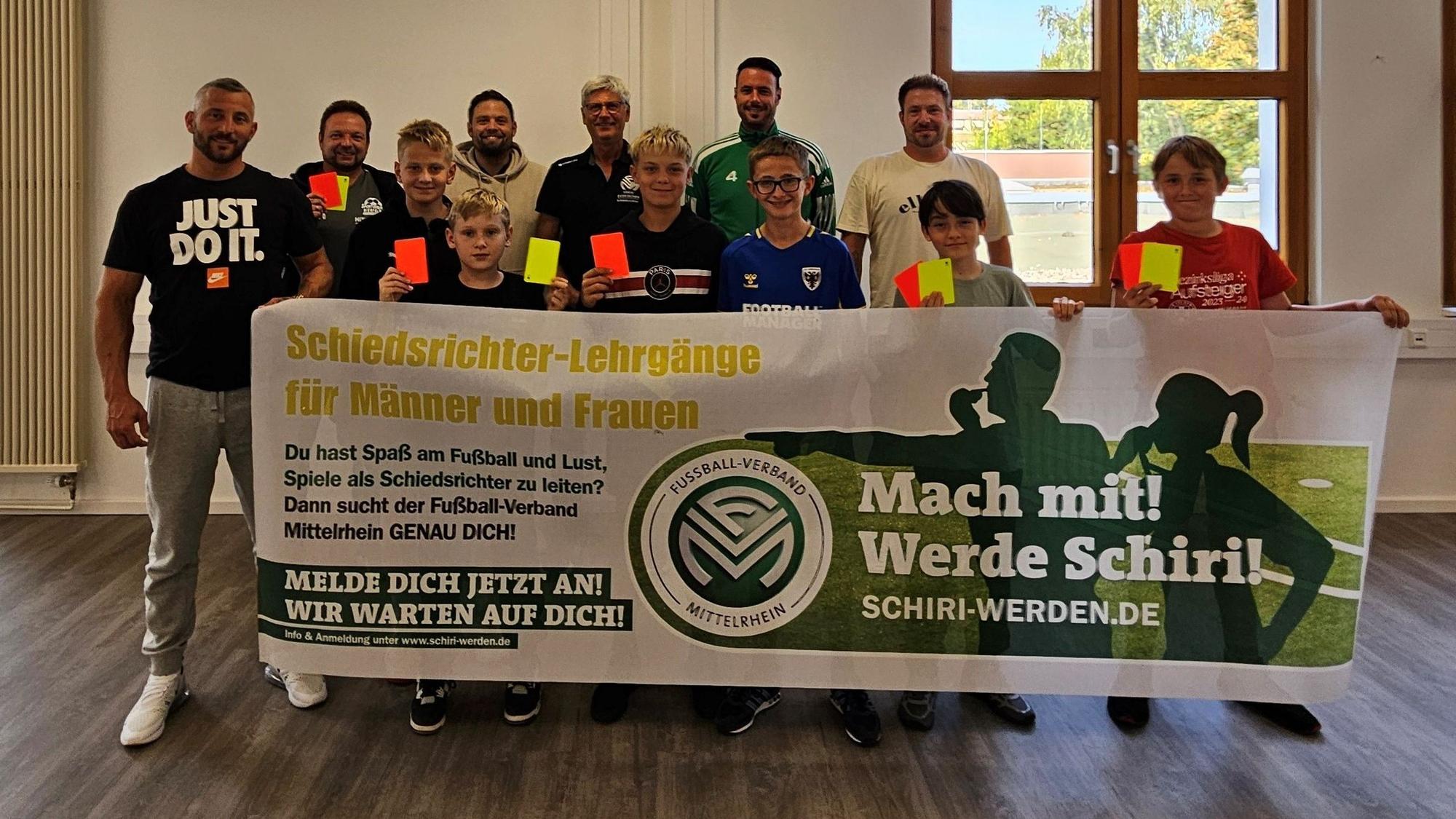 Die elf neuen Schiedsrichter und der Vorsitzende des Schiedsrichterausschuss halten Gelbe und Rote Karten ins Bild und ein Werbebanner für das Schiedsrichterwesen hoch.