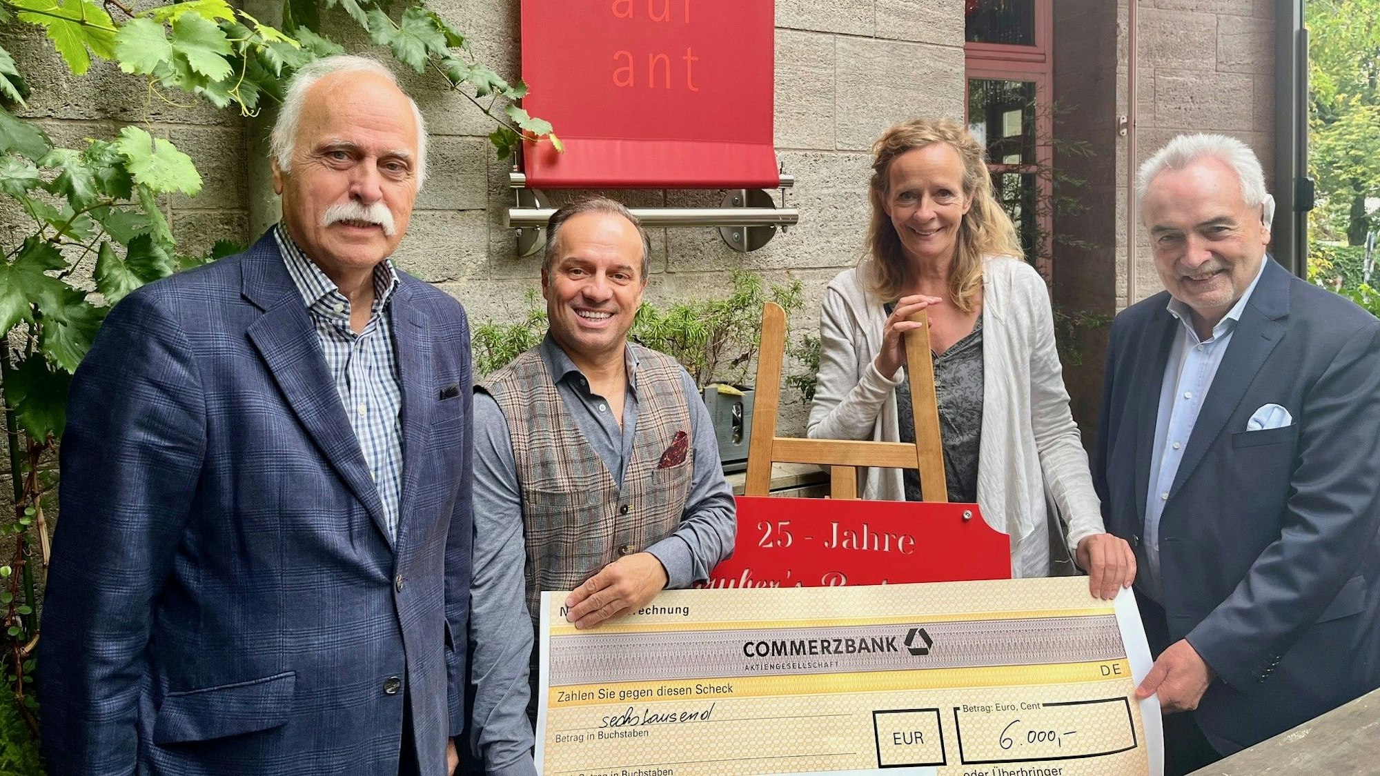 Franz A. Gruber (links) und Karl-Heinz Kappes (rechts) überreichen Isabella Neven DuMont und Karl-Heinz Goßmann von „wir helfen e.V.“ einen symbolischen Scheck in Höhe von 6000 Euro.