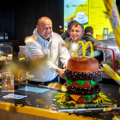 Das Bild zeigt, wie der Restaurant-Leiter und der Operations Manager im McDonald's in Euskirchen eine große BigMac-Torte anschneiden.
