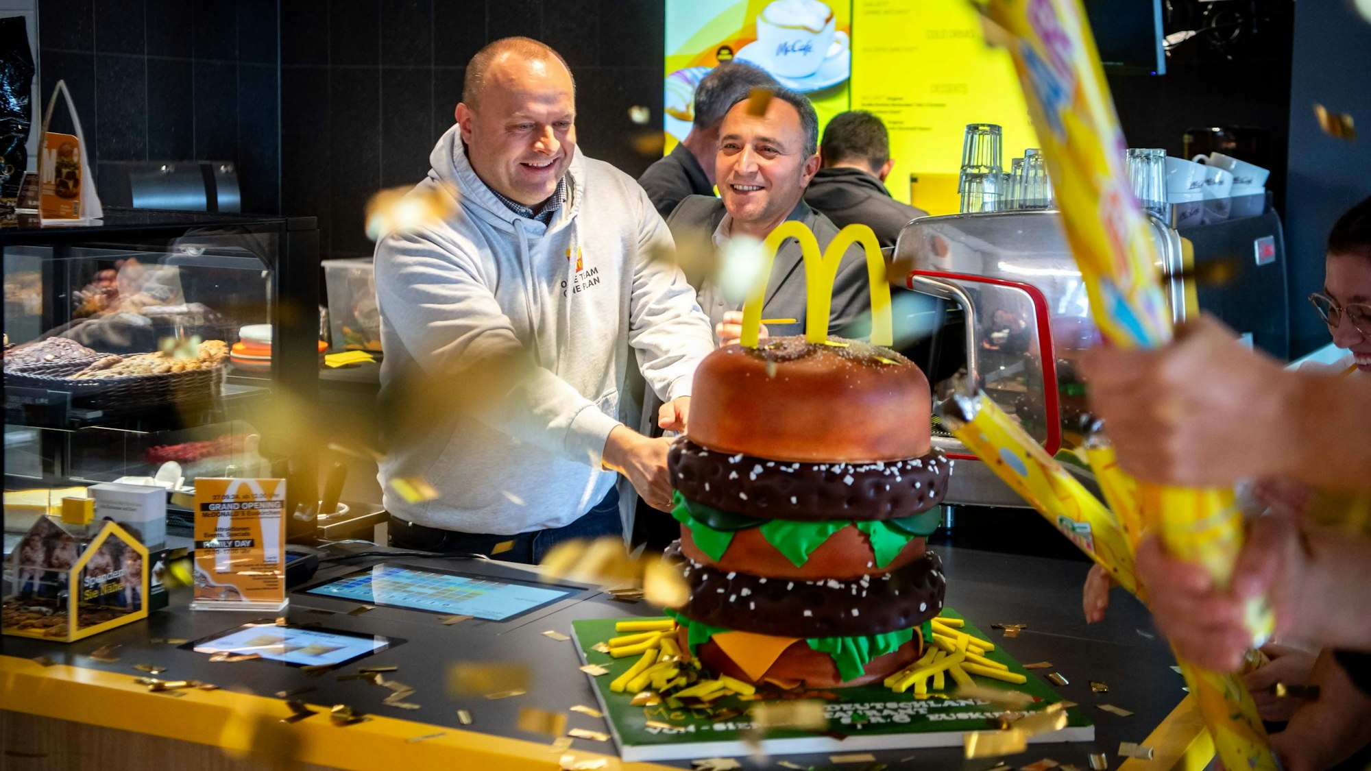 Das Bild zeigt, wie der Restaurant-Leiter und der Operations Manager im McDonald's in Euskirchen eine große BigMac-Torte anschneiden.