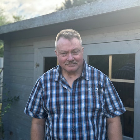 Werner Weisters hatte einen Schlaganfall und kam dank Frühreha wieder auf die Beine. Er steht im Karohemd vor einer Gartenlaube.