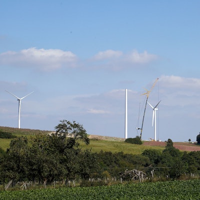 Auf einem Hügel bei Heimbach-Vlatten sind drei Windenergieanlagen zu sehen. Von einer vierten steht der Turm, mithilfe eines Krans wird daran gearbeitet.