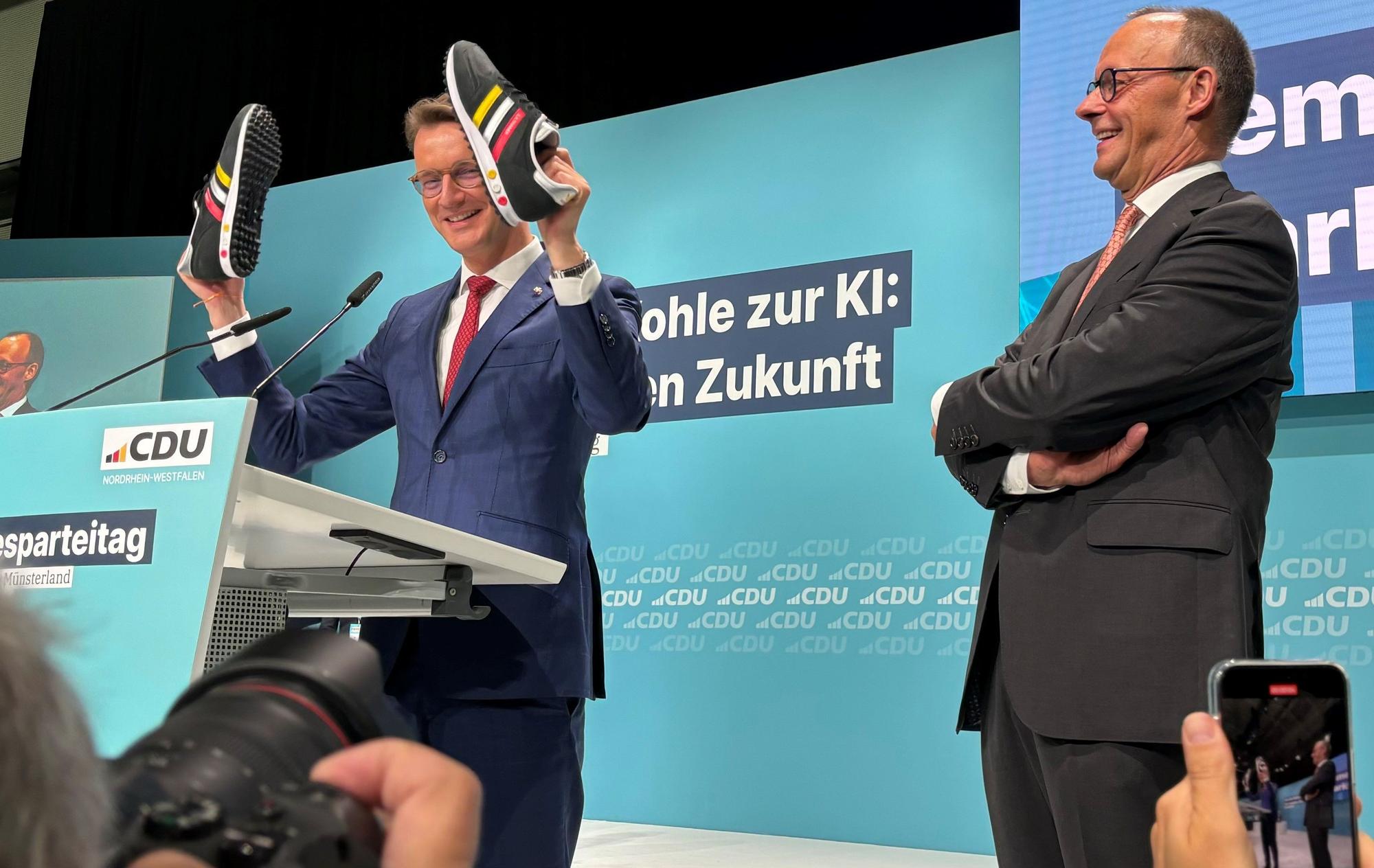 Hendrik Wüst schenkt Friedrich Merz beim CDU-Parteitag in Münster ein paar Turnschuhe.