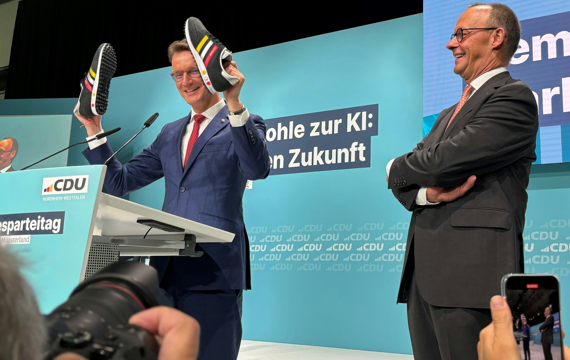 Hendrik Wüst schenkt Friedrich Merz beim CDU-Parteitag in Münster ein paar Turnschuhe.