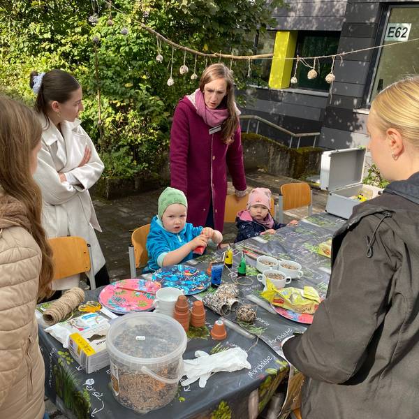 Kinder basteln an einem Tisch, dahinter stehen junge Frauen.