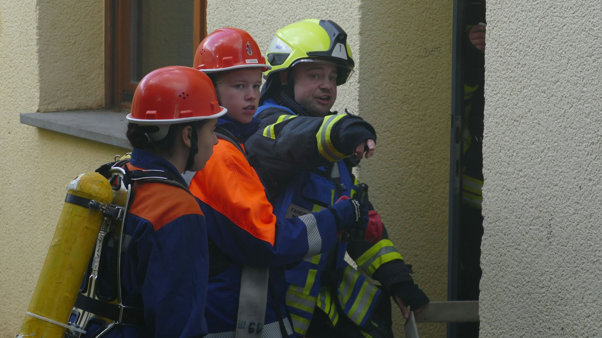 Zwei Jugendfeuerwehrleute und ein Feuerwehrmann vor einer Wand.