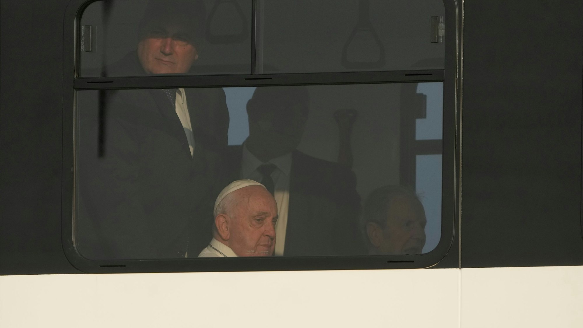 Papst Franziskus (M) sitzt in einem Shuttlebus zwischen seinen ständigern Begleitern, den Sicherheitsleuten.