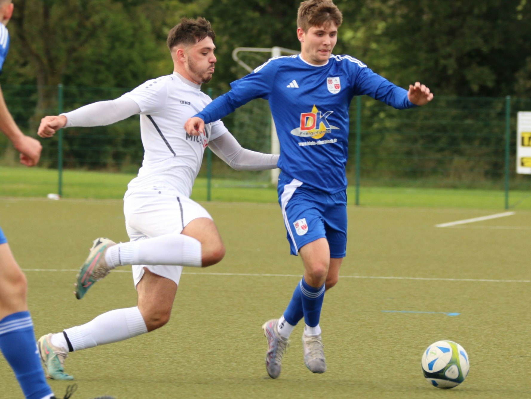 Ein Fußballer läuft mit einem Ball am Fuß, die Arme sind ausgestreckt, von hinten greift ein Gegenspieler an Es könnte weh tun.