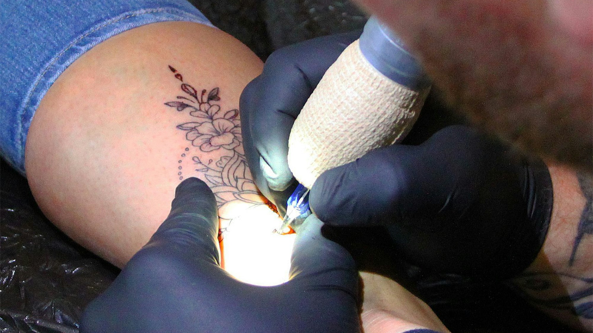Ein Mann sticht ein florales Tattoo auf einen Unterschenkel.