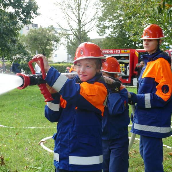 Drei Kinder der Jugendfeuerwehr Tropisdorf-Altenrath spritzen Wasser mit einem Schlauch.